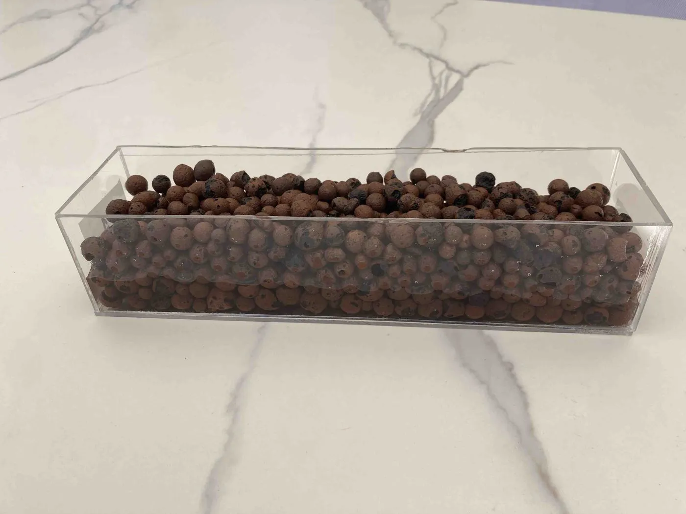 Clear rectangular planter filled with brown LECA clay pebbles, showing how shallow an 8 cm deep bed is