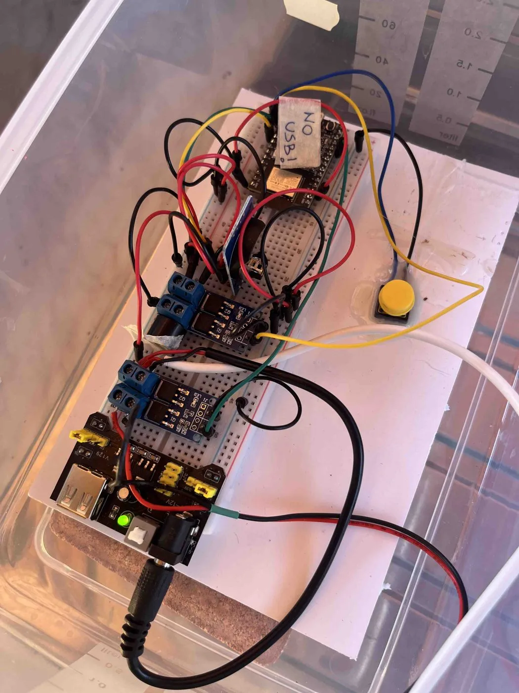 Homemade prototype controller on a breadboard inside a clear box, with colored jumper wires, two switch modules and a yellow push button