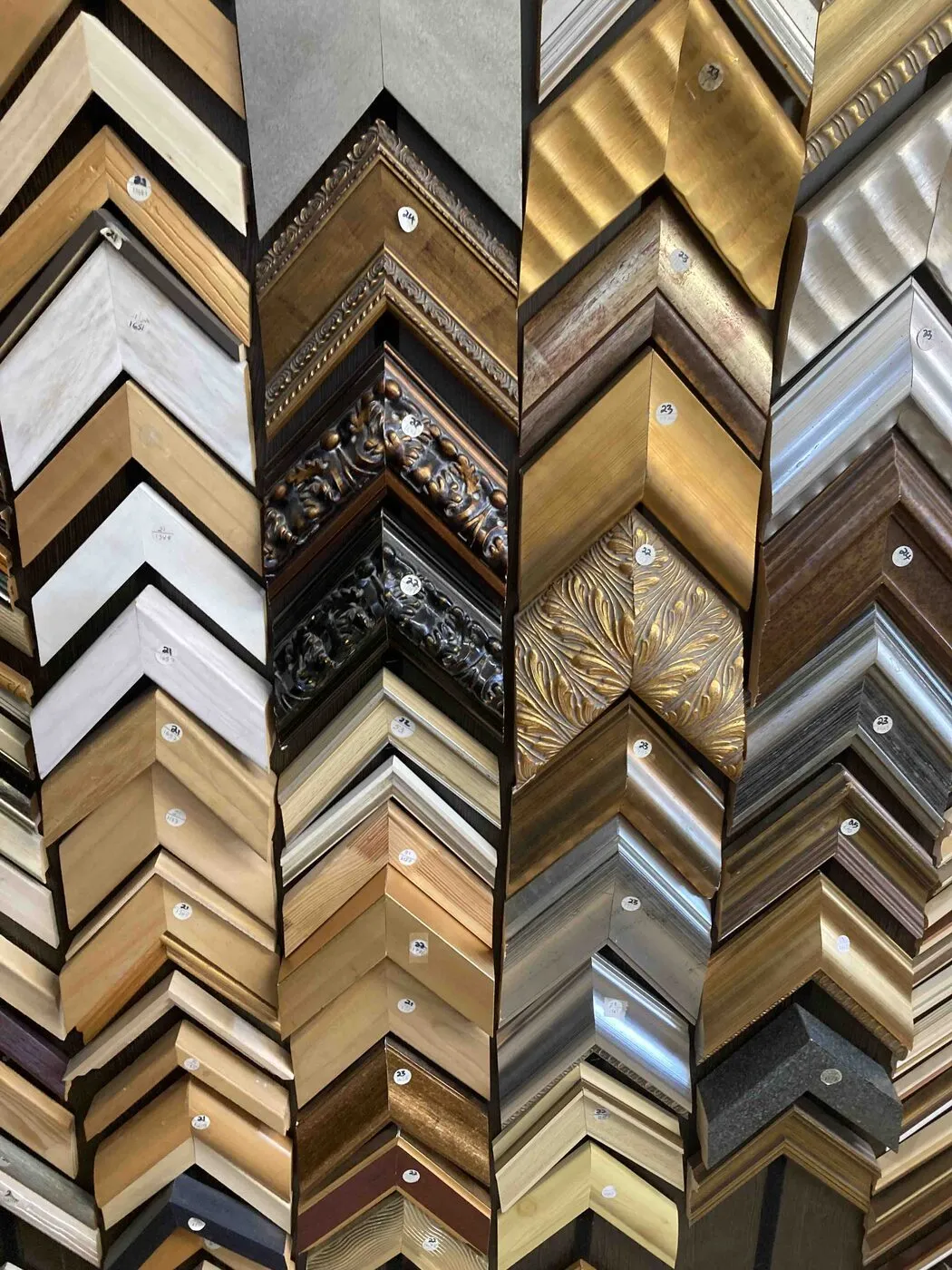 A wall of picture-frame corner samples in gold, silver, wood and black, arranged in chevrons.