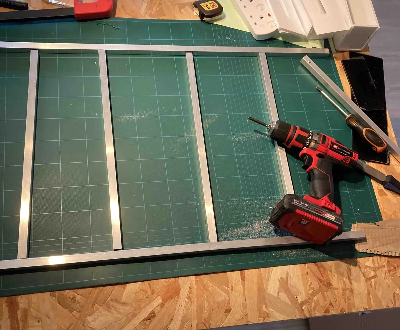Aluminum bars laid out as a ladder-shaped frame on the workbench, with a cordless drill.
