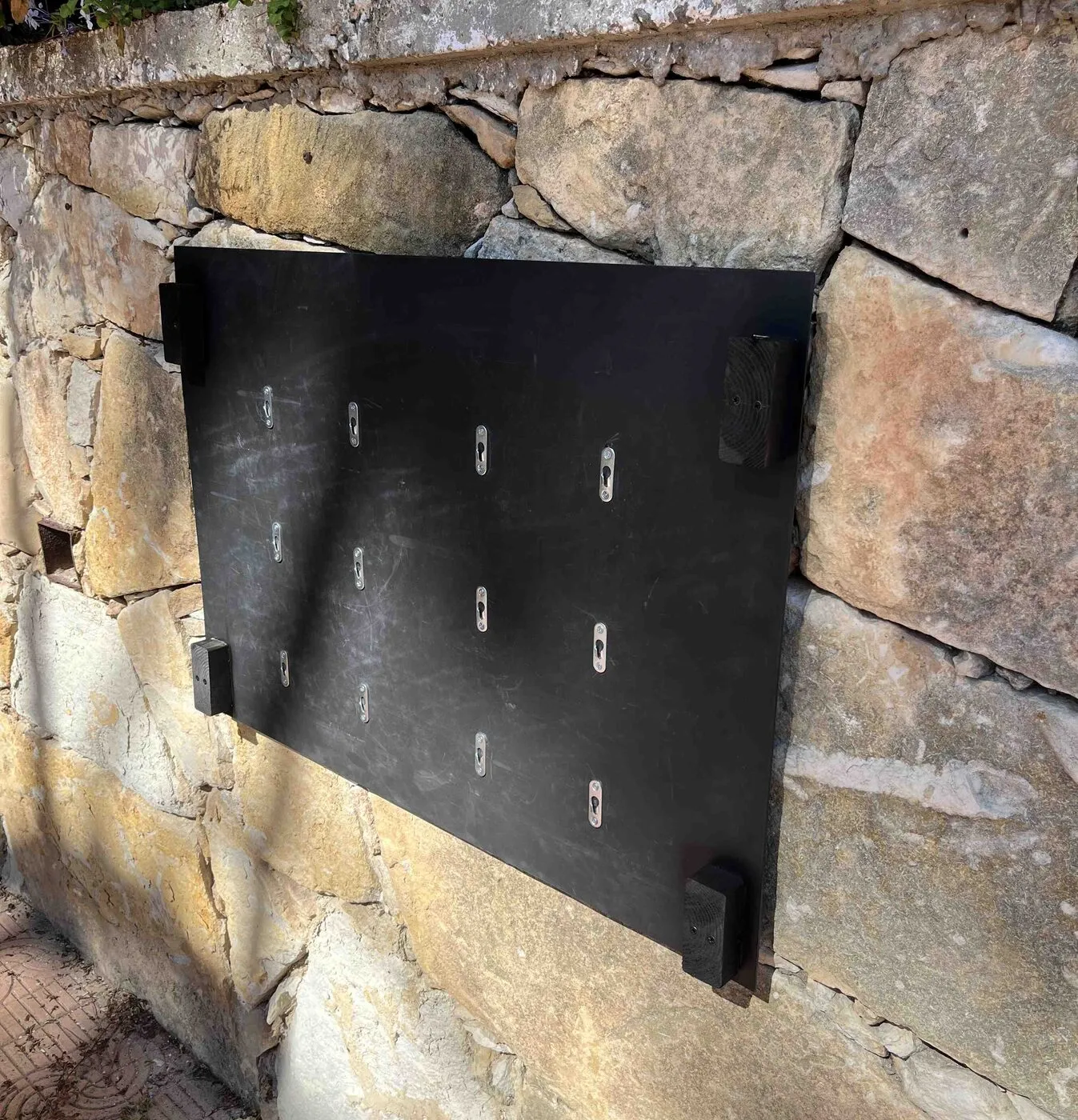 The bare black back panel hanging on a stone wall, its keyhole slots visible.