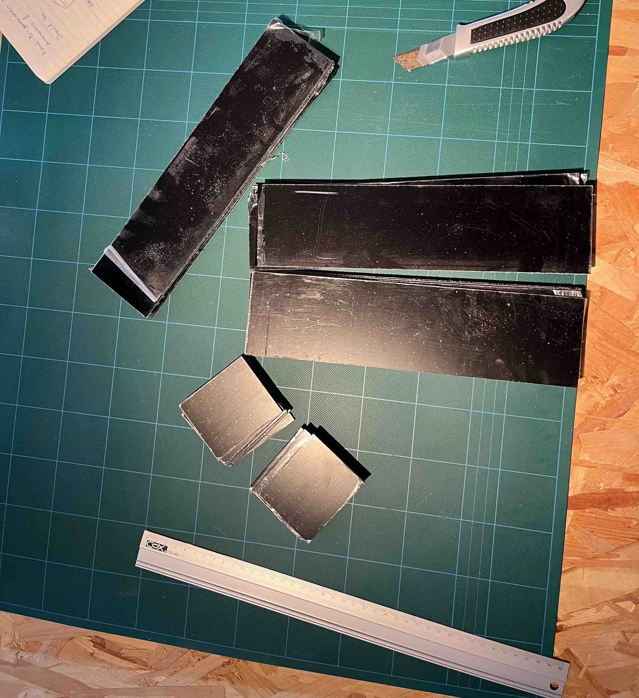A black acrylic planter being formed on a green cutting mat, with bent end pieces and a knife beside it.
