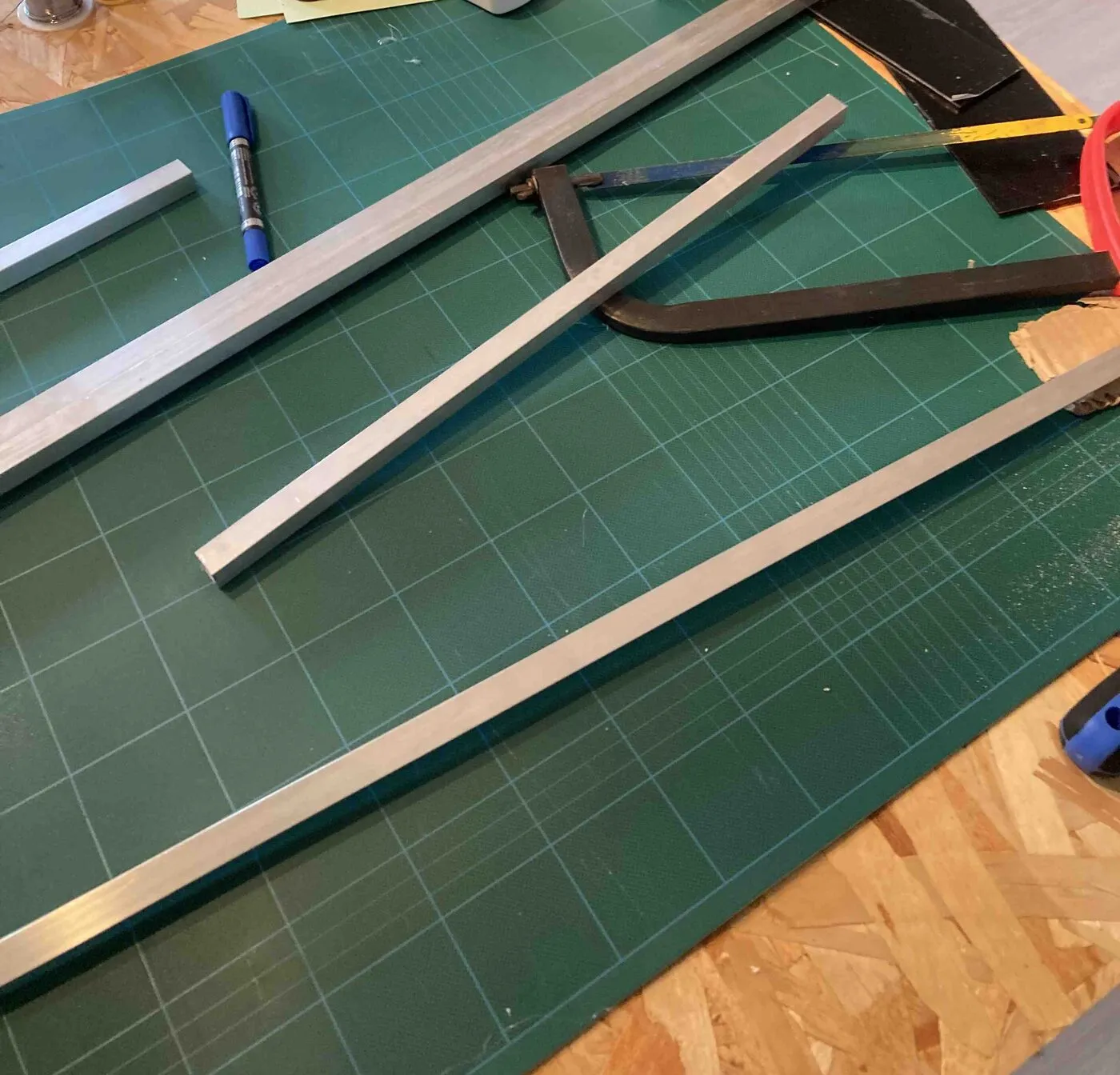 Aluminum bars and a hacksaw on a green cutting mat.