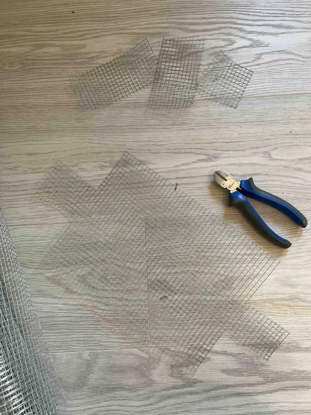 Pieces of wire mesh cut out on a wooden floor, with pliers.