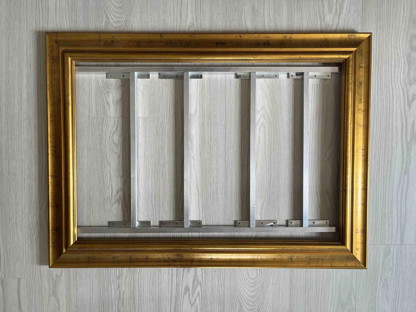 The gold frame laid on a light floor with the aluminum structure dry-fitted inside it.