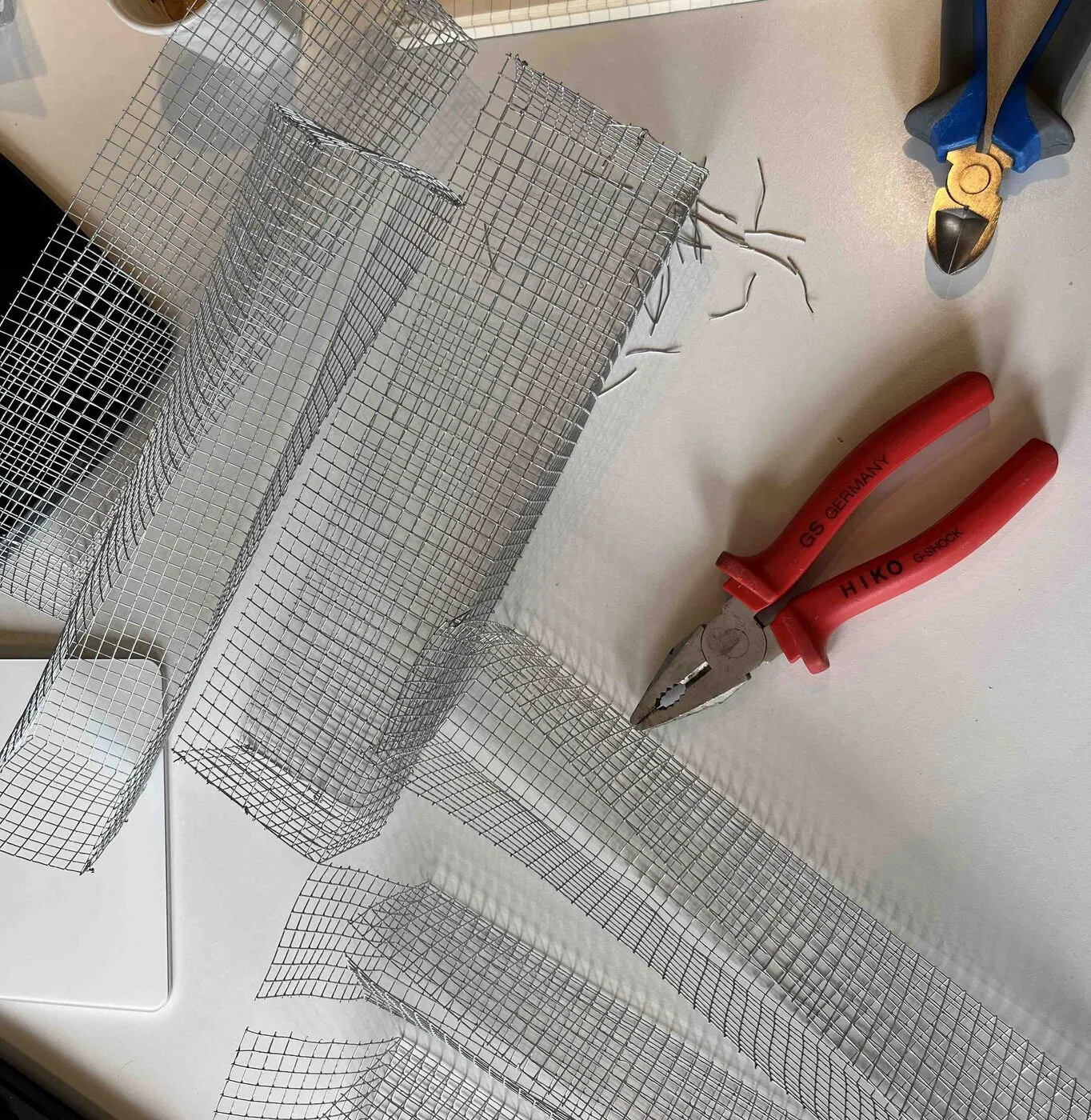 Wire mesh being folded into long narrow cups, with red pliers.
