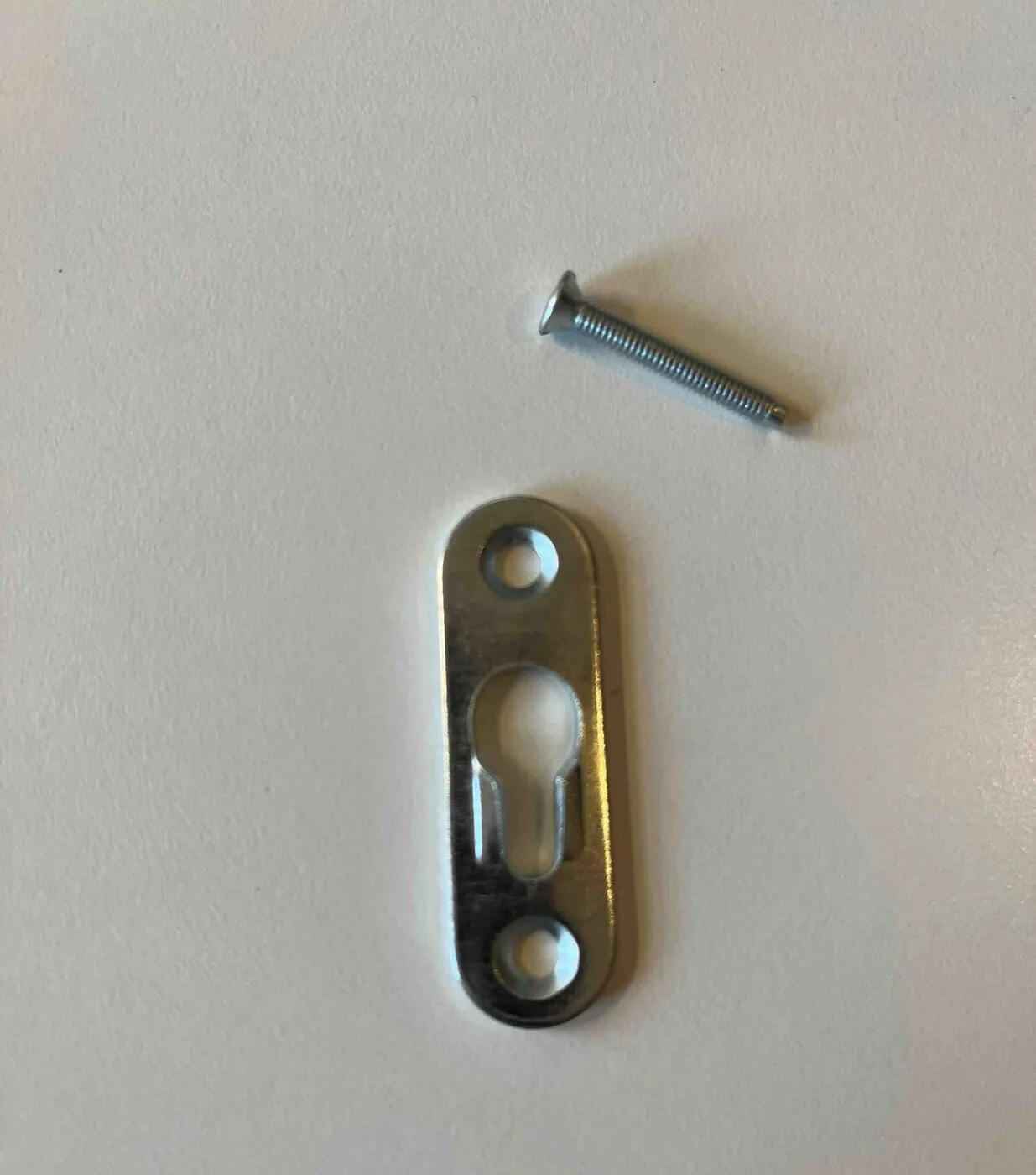 A small metal keyhole mounting plate and a screw on a white surface.