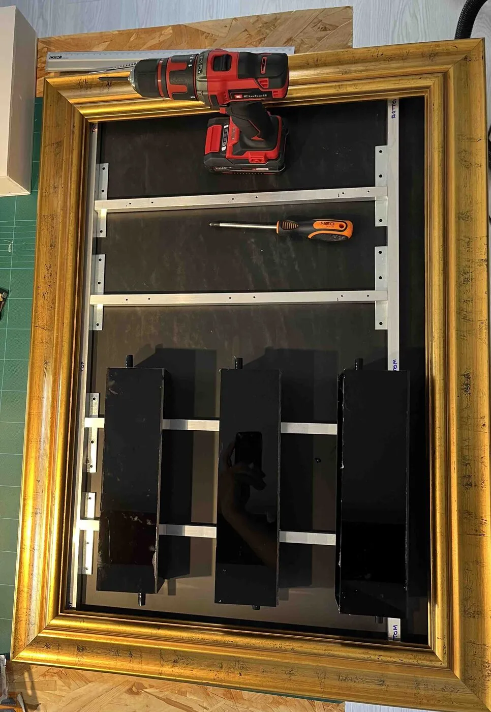 The gold frame on the workbench with the aluminum structure inside and the first black planters in place.