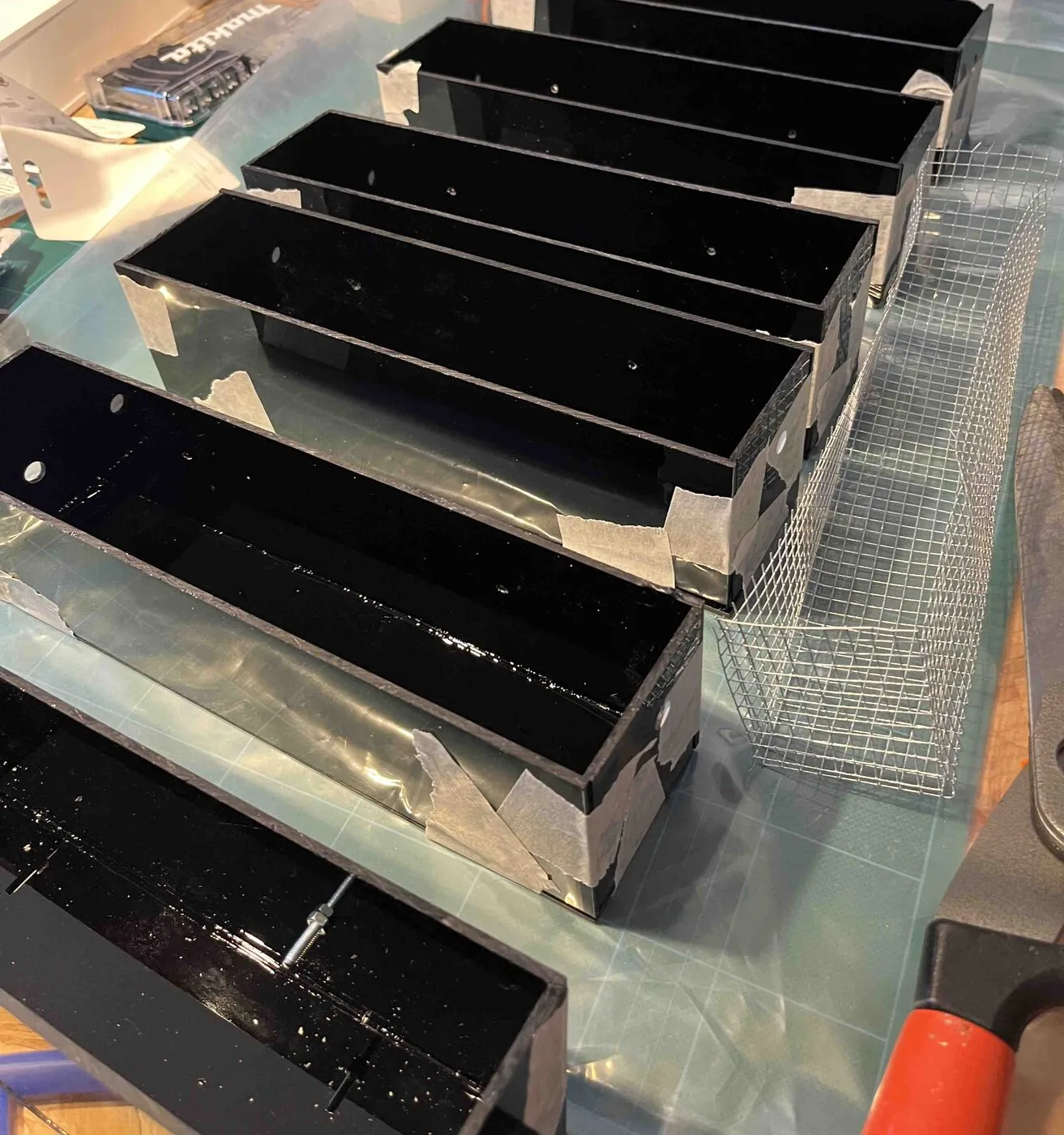 Six finished black acrylic planters lined up on a workbench.