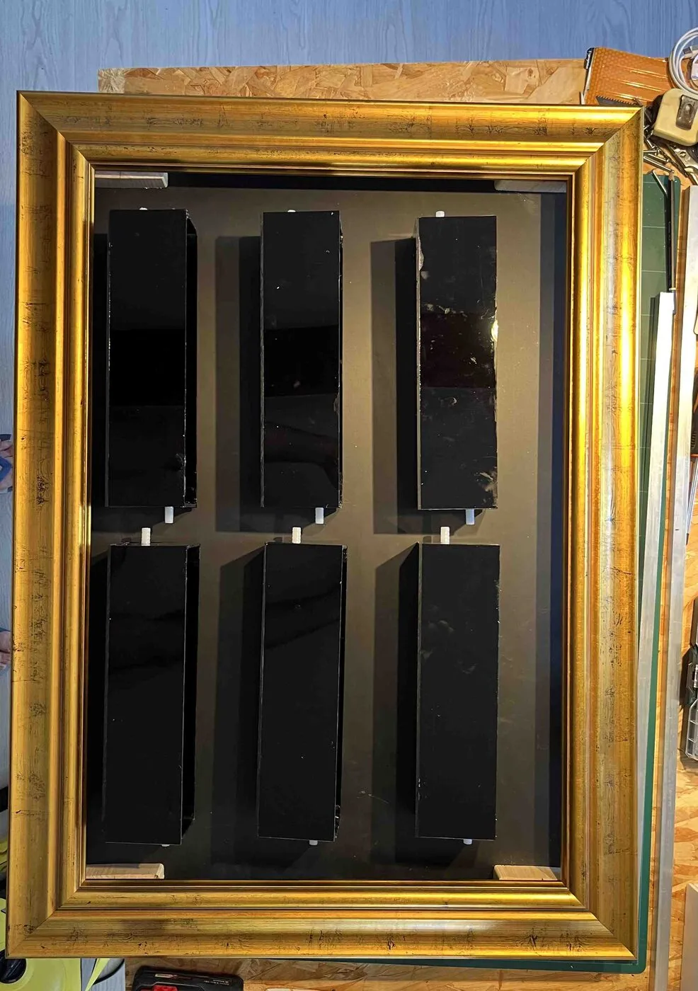 All six black planters in place inside the gold frame, seen from above on the workbench.